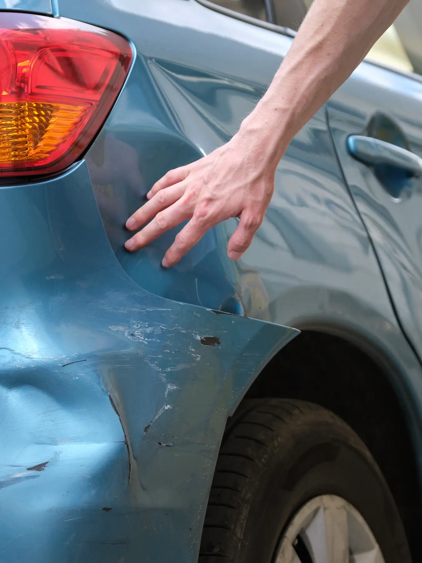 Nahaufnahme Hand zeigt auf Delle am blauen Fahrzeugheck in Solingen